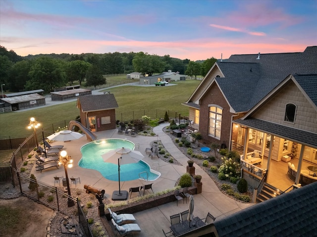 pool at dusk with a lawn, an outbuilding, a patio area, and a water slide