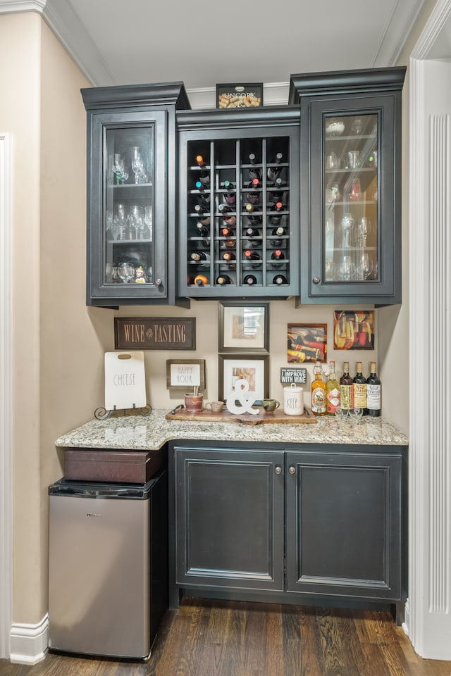 bar with dark wood-type flooring, light stone countertops, ornamental molding, and refrigerator