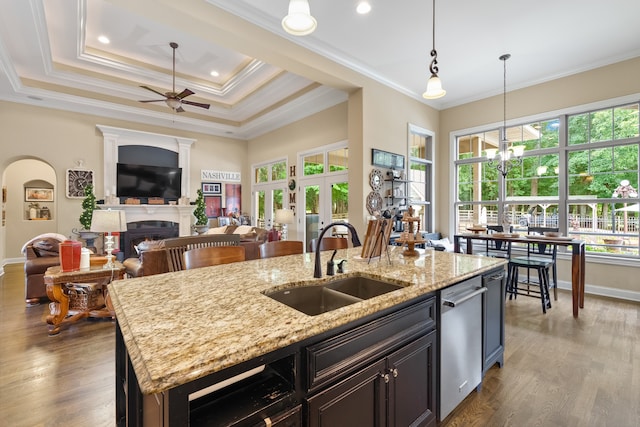 kitchen with crown molding, a kitchen island with sink, dishwasher, ceiling fan, and wood-type flooring