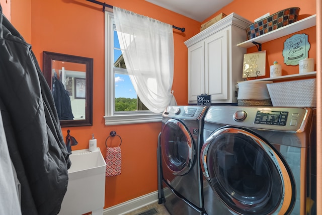 clothes washing area featuring washing machine and clothes dryer and cabinets