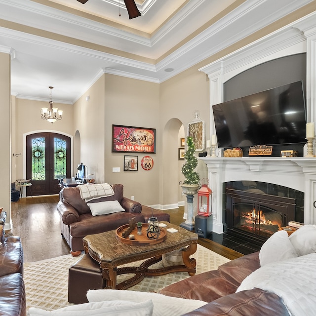 living room featuring dark hardwood / wood-style flooring, ceiling fan with notable chandelier, crown molding, french doors, and a tiled fireplace