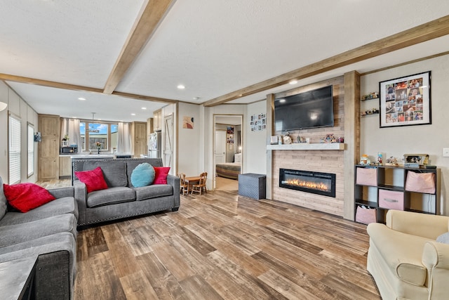 living room featuring a stone fireplace, a textured ceiling, beam ceiling, brick wall, and hardwood / wood-style flooring