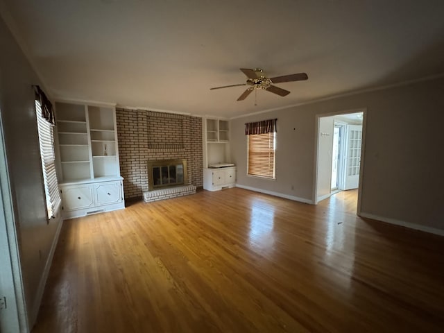 unfurnished living room with hardwood / wood-style flooring, ceiling fan, crown molding, and a brick fireplace