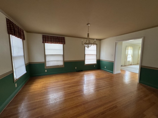 unfurnished dining area featuring hardwood / wood-style flooring, ornamental molding, and a notable chandelier