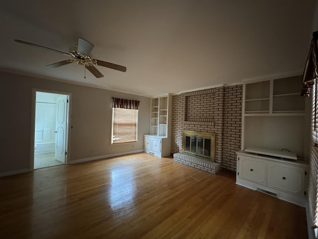 unfurnished living room with ornamental molding, ceiling fan, hardwood / wood-style flooring, built in features, and a fireplace