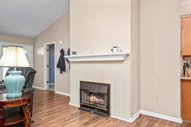 living room with a tile fireplace, hardwood / wood-style flooring, and lofted ceiling