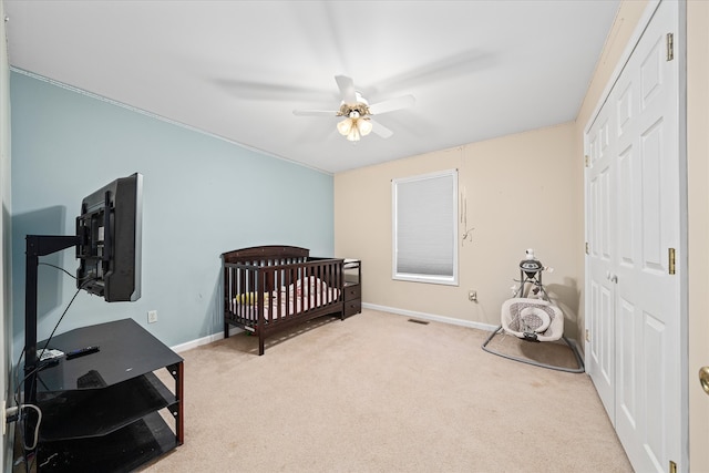 bedroom with a crib, ceiling fan, light colored carpet, a closet, and ornamental molding