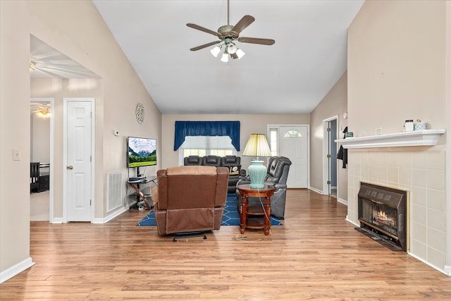 living room with ceiling fan, a fireplace, light hardwood / wood-style flooring, and vaulted ceiling