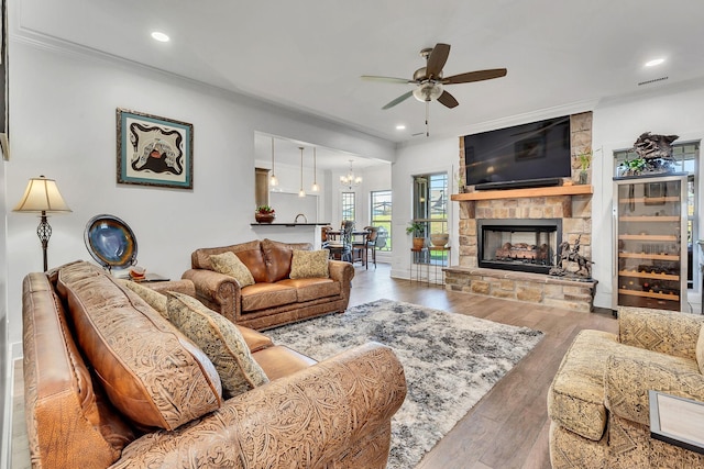 living room with hardwood / wood-style flooring, ceiling fan, ornamental molding, and a stone fireplace