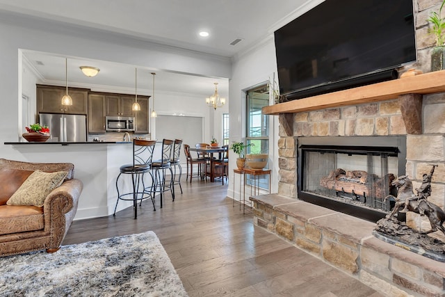 living room featuring crown molding, dark wood-type flooring, a stone fireplace, and a chandelier