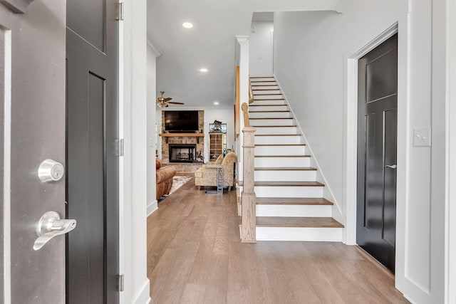 foyer entrance with a stone fireplace, ceiling fan, and light hardwood / wood-style flooring