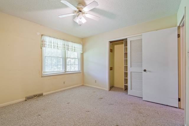 unfurnished bedroom featuring light carpet, a textured ceiling, a closet, and ceiling fan