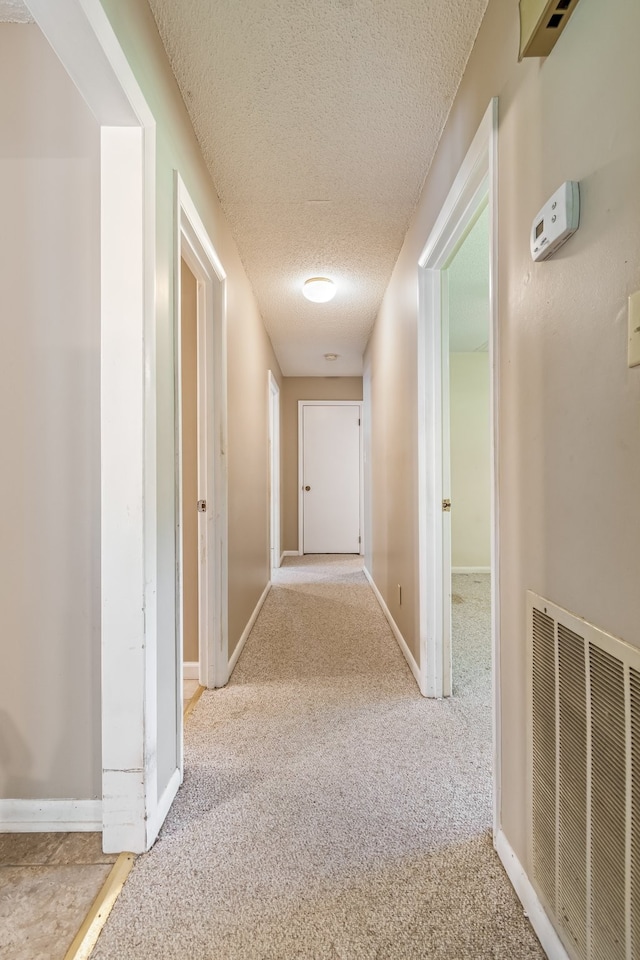 hall featuring a textured ceiling and light colored carpet