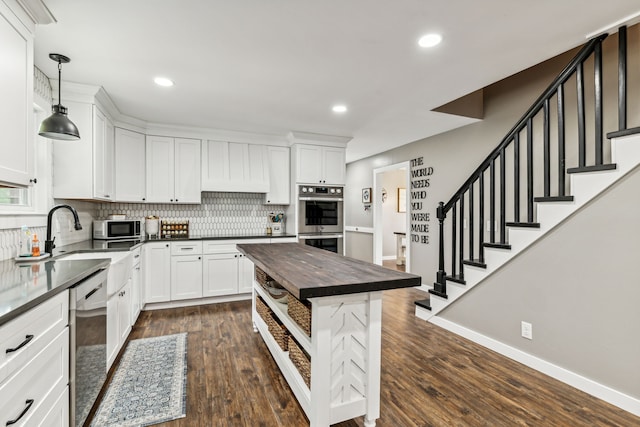 kitchen featuring dishwashing machine, butcher block counters, dark wood-type flooring, double oven, and hanging light fixtures