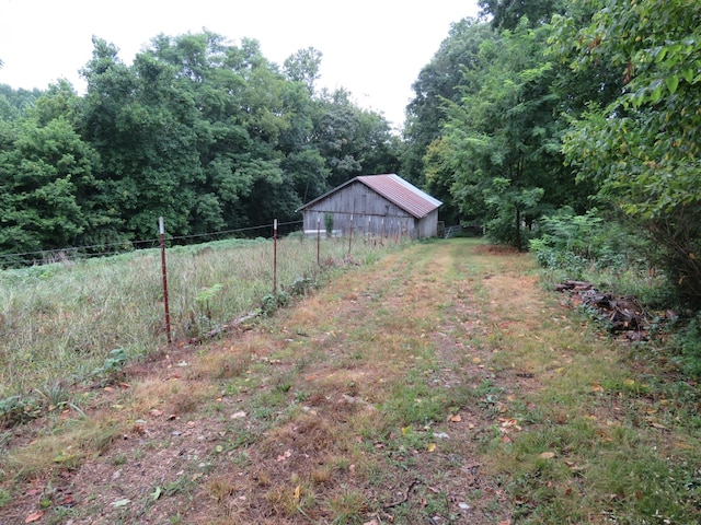 view of yard with an outbuilding, a pole building, fence, and a view of trees