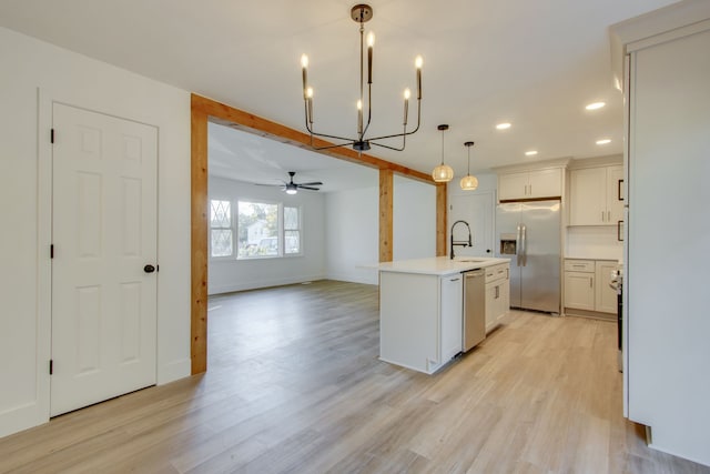 kitchen with light wood-type flooring, a center island with sink, stainless steel appliances, hanging light fixtures, and white cabinets