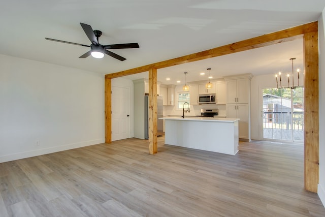 unfurnished living room with ceiling fan with notable chandelier, beamed ceiling, sink, and light hardwood / wood-style floors