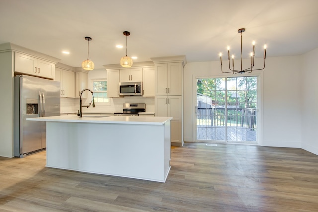 kitchen with light hardwood / wood-style floors, pendant lighting, a center island with sink, sink, and stainless steel appliances