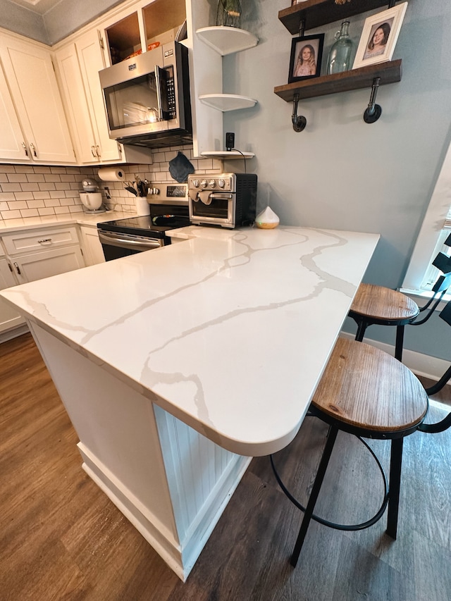 kitchen with white cabinets, backsplash, light stone countertops, hardwood / wood-style floors, and appliances with stainless steel finishes