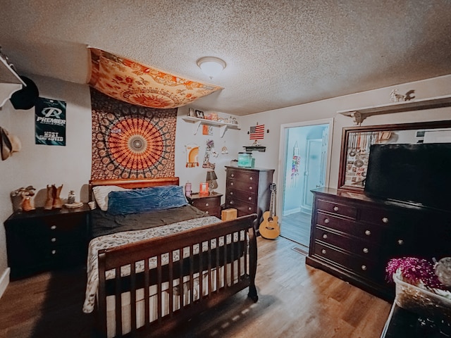 bedroom with ensuite bath, light wood-type flooring, and a textured ceiling