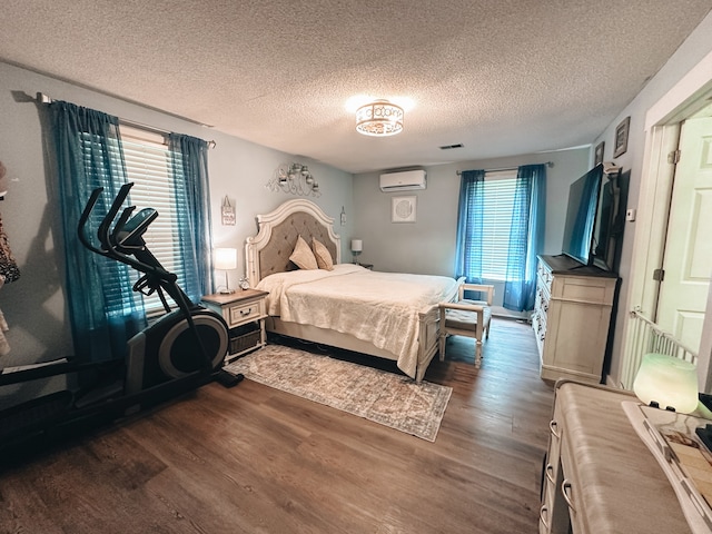 bedroom with a wall mounted AC, dark hardwood / wood-style flooring, and a textured ceiling