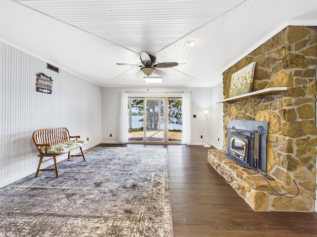 sitting room with dark wood-type flooring, a wood stove, and ceiling fan