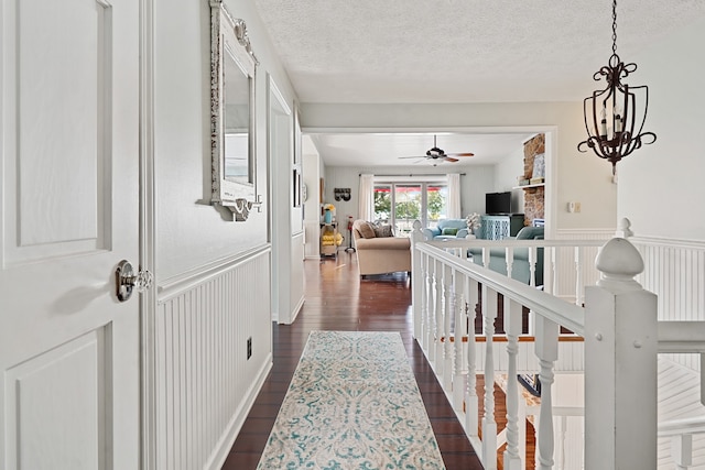 hall featuring dark wood-type flooring, a notable chandelier, and a textured ceiling