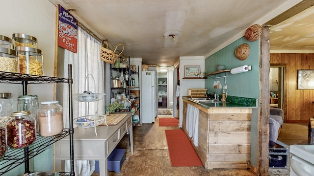 kitchen featuring white refrigerator, sink, and wooden walls