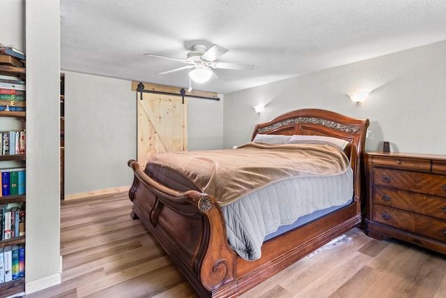 bedroom with a textured ceiling, ceiling fan, a barn door, and light hardwood / wood-style flooring