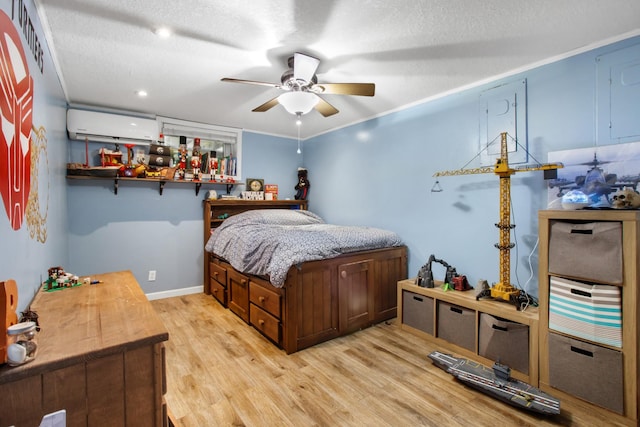 bedroom featuring a textured ceiling, light hardwood / wood-style floors, ornamental molding, ceiling fan, and a wall mounted air conditioner