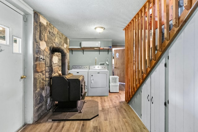 laundry room featuring a textured ceiling, light hardwood / wood-style floors, a wood stove, and washing machine and clothes dryer