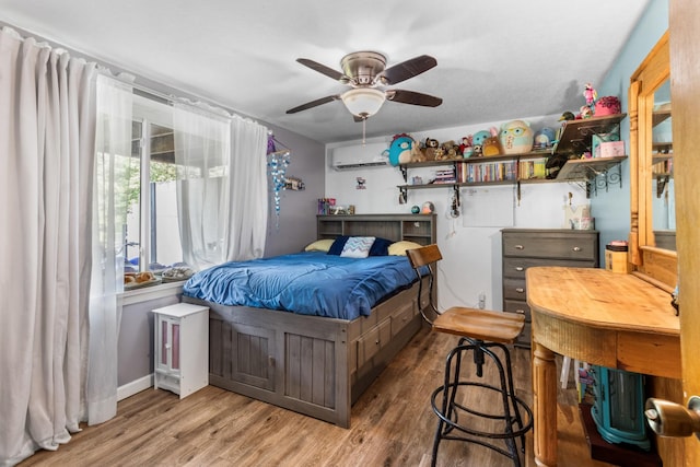 bedroom featuring ceiling fan, a wall mounted air conditioner, and hardwood / wood-style floors