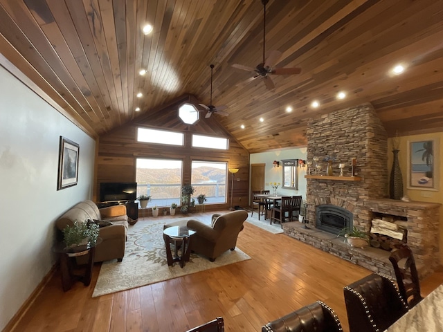 living room with hardwood / wood-style flooring, ceiling fan, high vaulted ceiling, a stone fireplace, and wooden ceiling