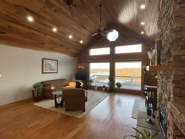 living room with a stone fireplace, a towering ceiling, hardwood / wood-style floors, ceiling fan, and wooden ceiling