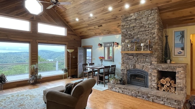 living room featuring a stone fireplace, high vaulted ceiling, light wood-type flooring, wooden ceiling, and a mountain view