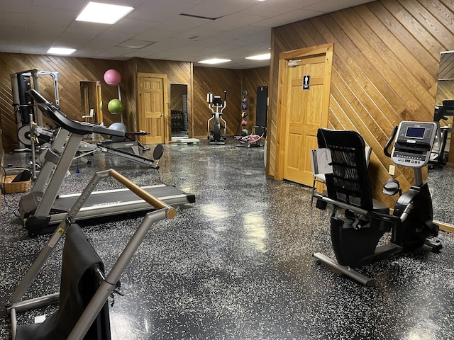 exercise room featuring a paneled ceiling and wooden walls