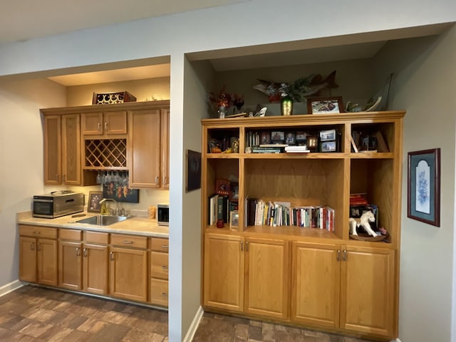 bar featuring stone finish floor, a sink, stainless steel microwave, a toaster, and baseboards