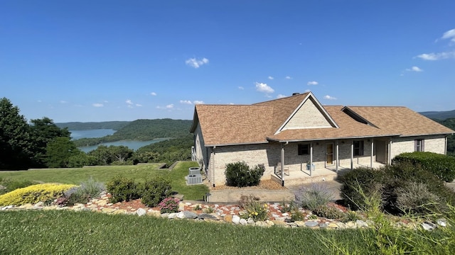 view of home's exterior with a water view, a yard, roof with shingles, brick siding, and a patio area