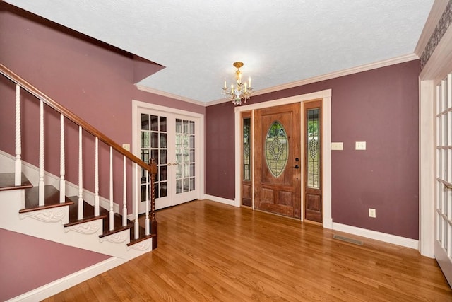 foyer with crown molding, hardwood / wood-style floors, a chandelier, and french doors