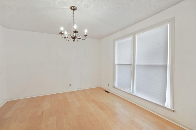 spare room featuring light wood-style floors, visible vents, a textured ceiling, and an inviting chandelier