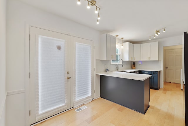 kitchen with light wood-type flooring, sink, pendant lighting, and white cabinets