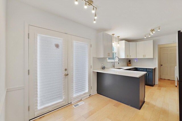 kitchen with tasteful backsplash, visible vents, light wood-style flooring, a peninsula, and a sink