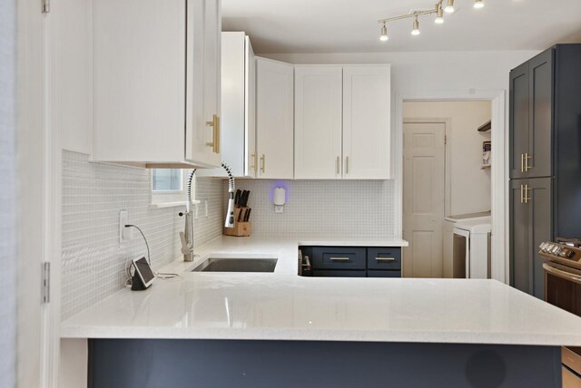 kitchen with backsplash, white cabinets, a sink, washer / dryer, and a peninsula