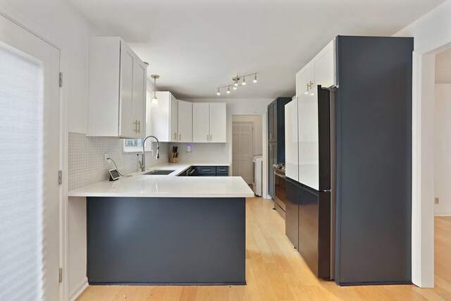 kitchen featuring light countertops, decorative backsplash, light wood-style floors, a sink, and a peninsula