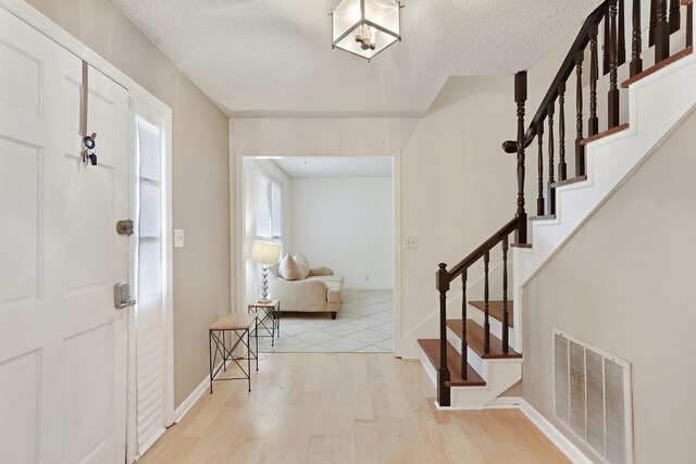 entryway with stairs, visible vents, a textured ceiling, and wood finished floors