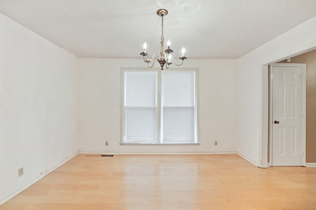 unfurnished room with a notable chandelier, a textured ceiling, and light wood-type flooring