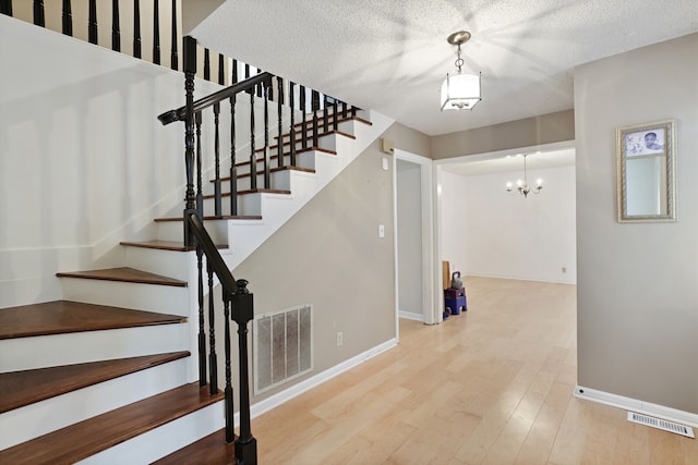 staircase featuring a textured ceiling, a notable chandelier, and hardwood / wood-style flooring