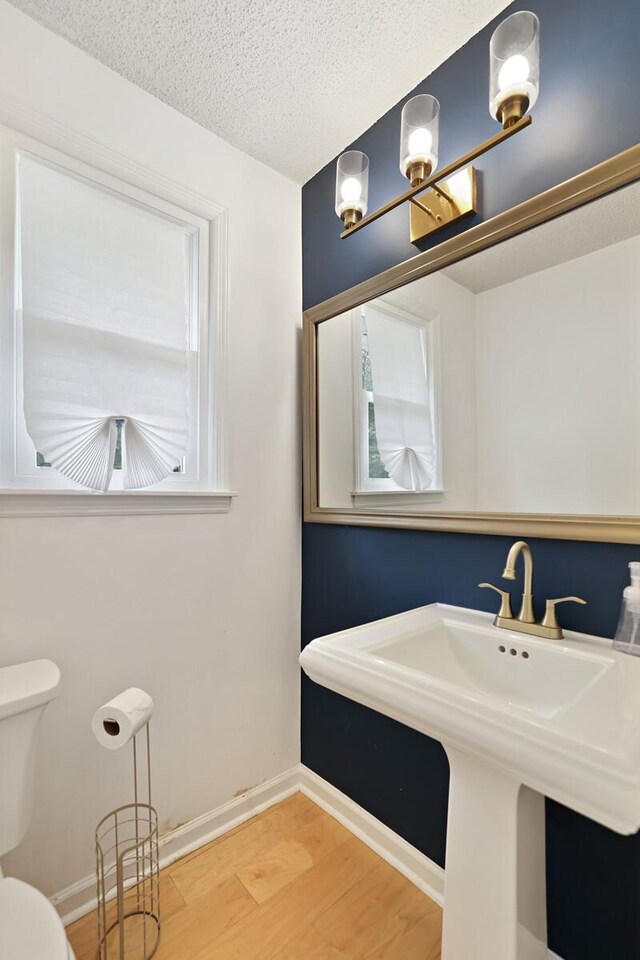 half bath featuring toilet, a sink, a textured ceiling, wood finished floors, and baseboards