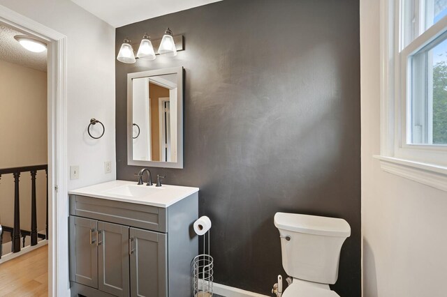 half bathroom featuring wood finished floors, vanity, and toilet