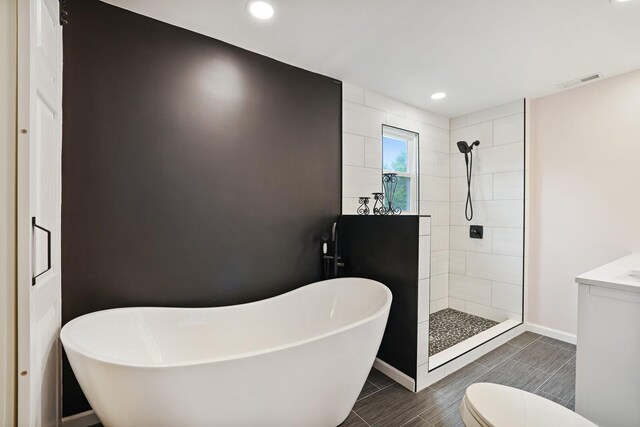 bathroom featuring baseboards, visible vents, tiled shower, toilet, and a freestanding bath